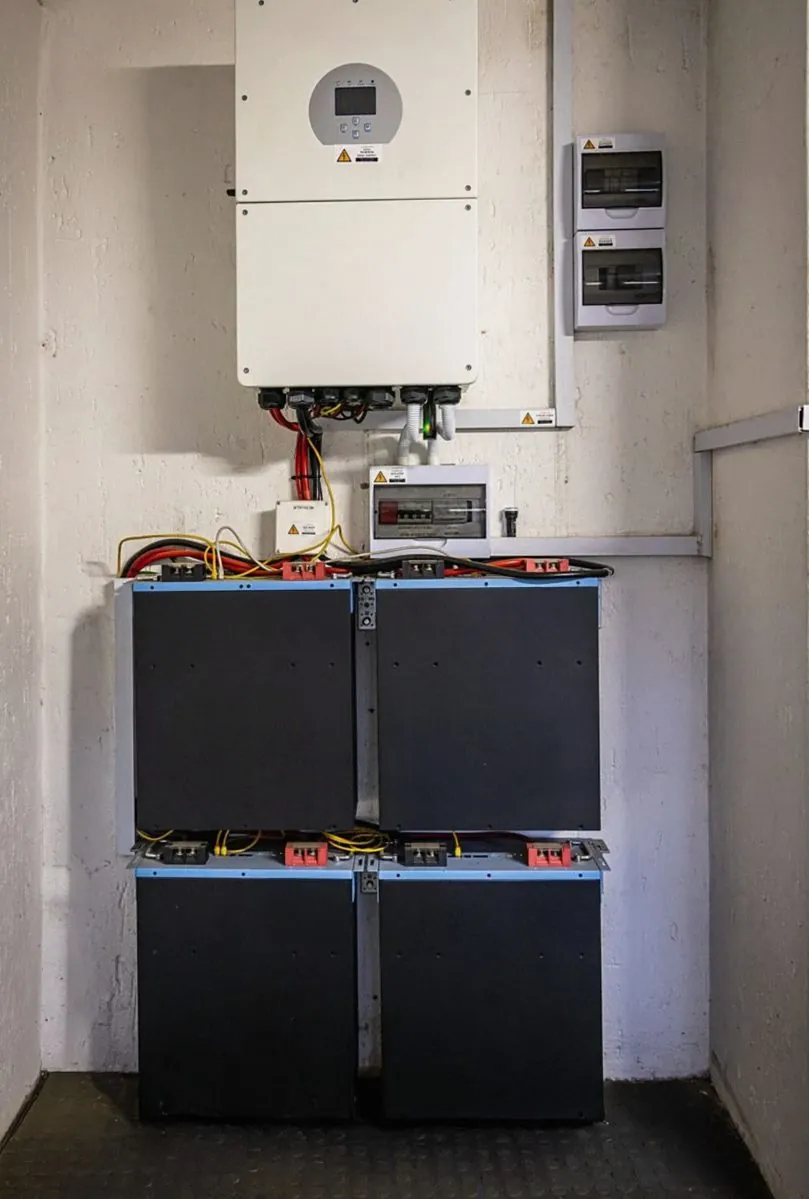 Wall-mounted hybrid inverter above a stack of home battery modules in a utility cupboard (illustrative photo)