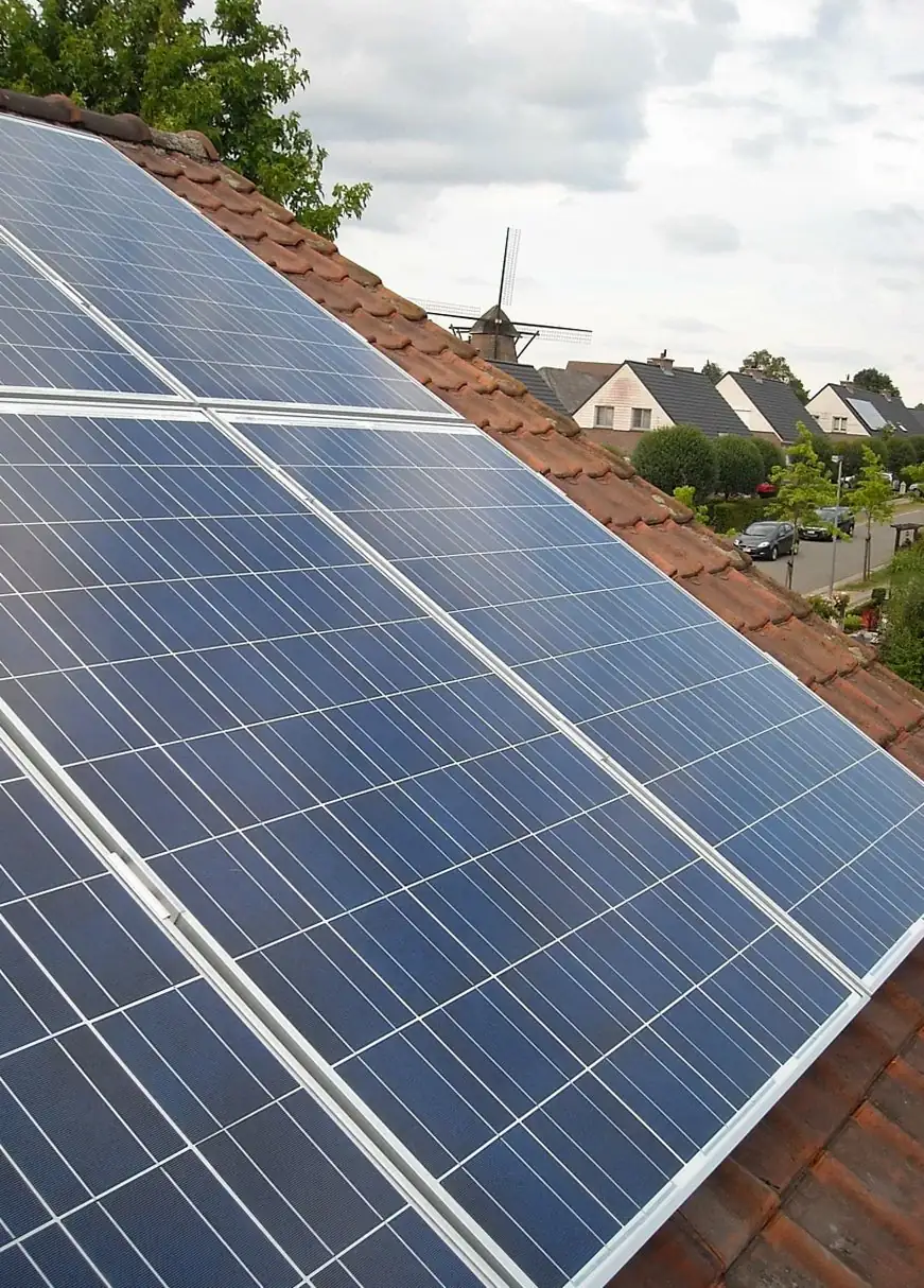 Solar panels on a red tiled roof with a row of houses in the distance (illustrative photo)