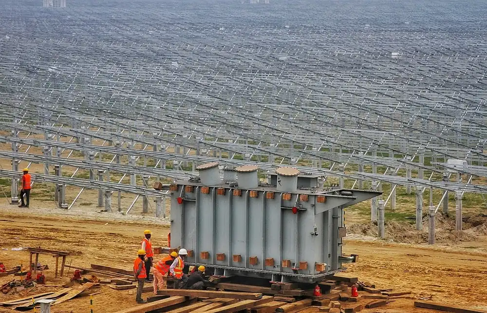 Construction crew in orange vests beside a large transformer at a ground-mounted solar power plant site (illustrative photo)